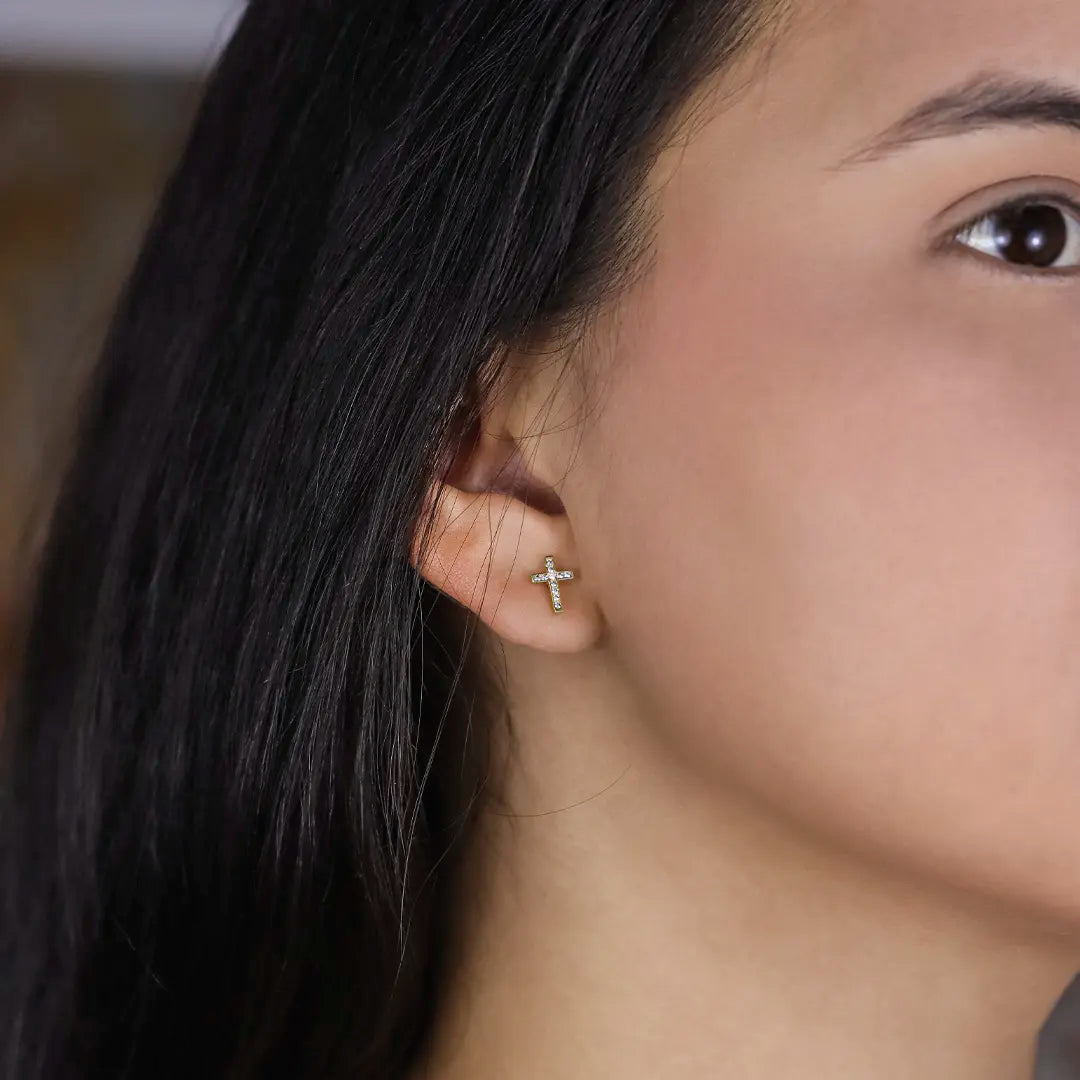 Oreja de mujer con topito en forma de cruz en oro amarillo de 18 quilates con cristales de color blanco, hechos en Joyería Caracas. 