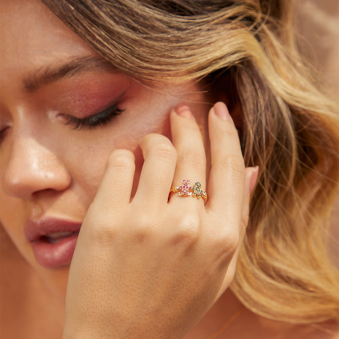 Mano de mujer usando anillo con forma de niño y niña en oro amarillo de 18 quilates con cristales de color verde y rosa, hecho en Joyería Caracas. 