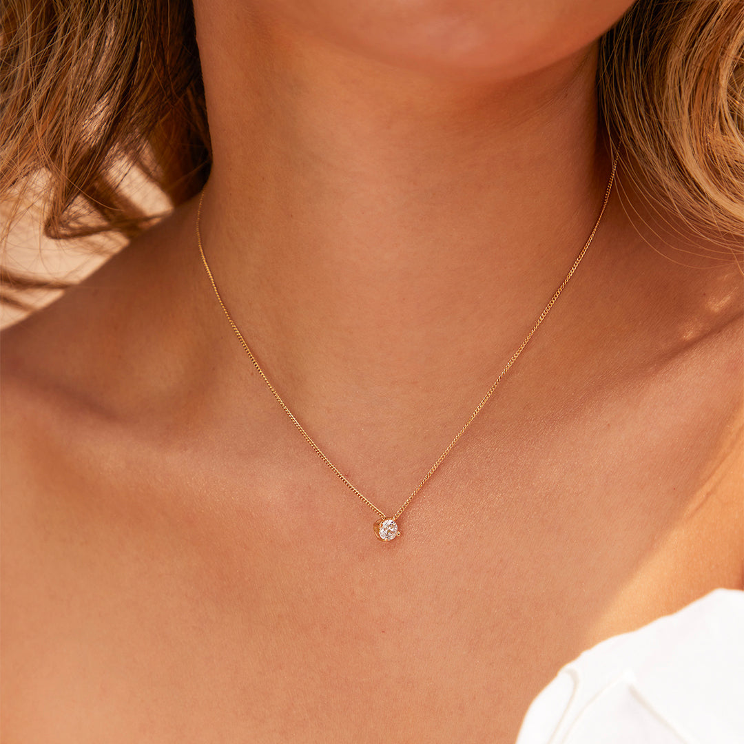 Cuello de mujer usando gargantilla mini cubana con dije pasante en oro amarillo de 18 quilates con cristal de color blanco, hecho en Joyería Caracas. 