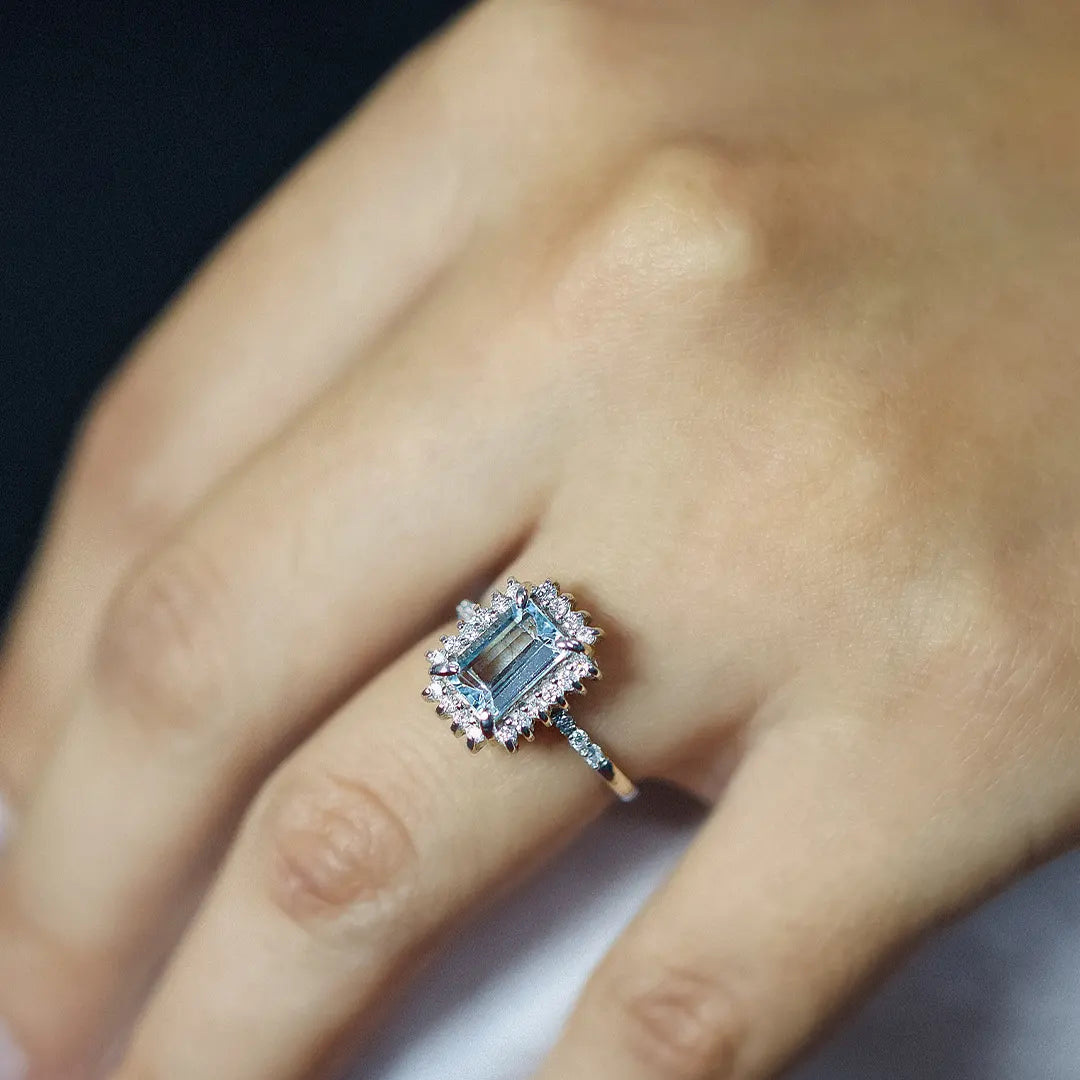 Mano de mujer con un anillo en oro blanco de 18 quilates con una piedra de color celeste de topacio y alrededor de ella diamantes de color blanco, hecho en Joyería Caracas.