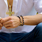Mano de hombre con pulsera tejida en hilo negro, bisutería, esferas diamantadas y dije de calavera en oro amarillo de 18 quilates con cristales de color blanco y negro, hecho en Joyería Caracas. 