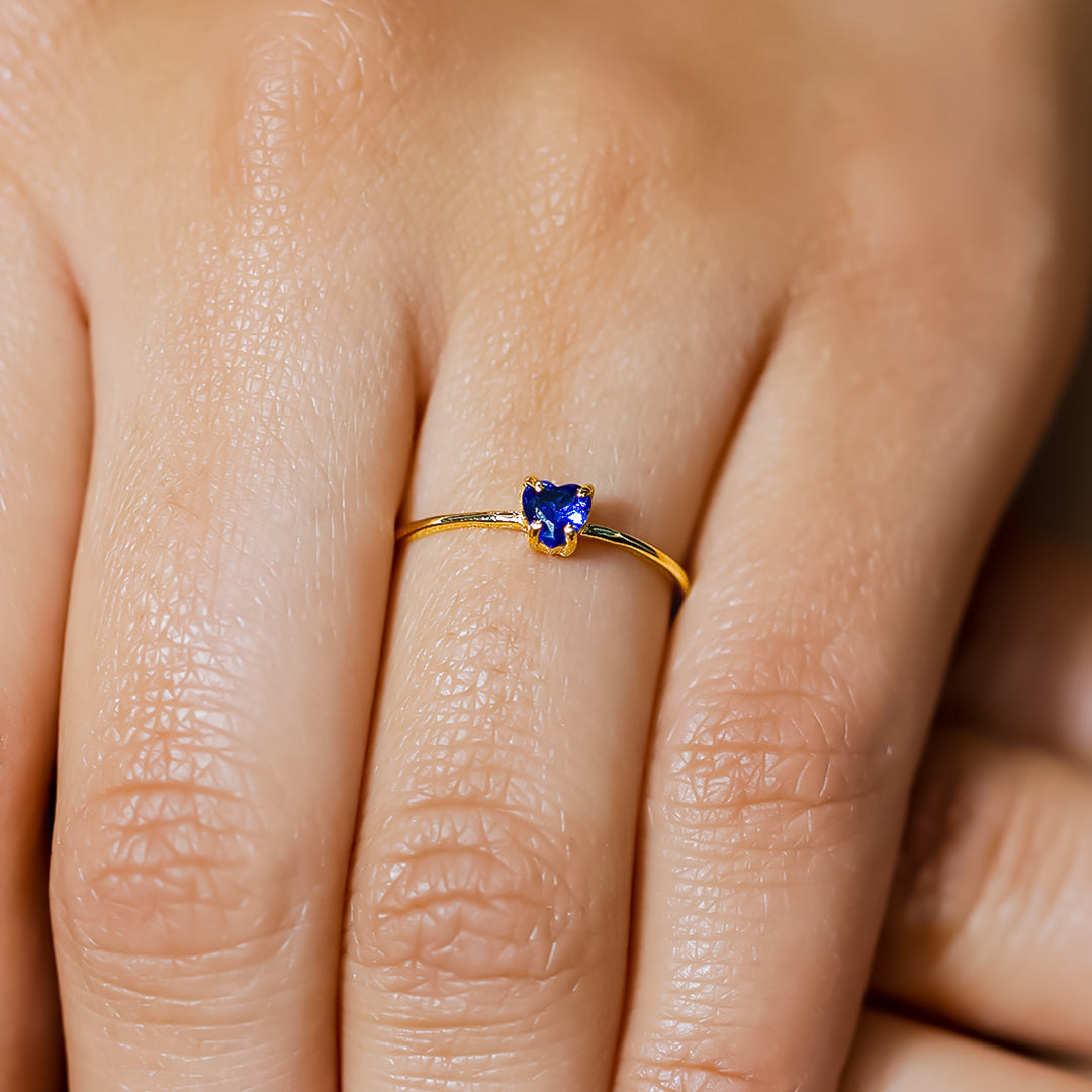 Mano de mujer con anillo en oro amarillo de 18 quilates con cristal de color azul en forma de corazón, hecho en Joyería Caracas. 