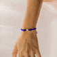 Mano de mujer con pulsera tejida en hilo azul coreano, bisutería y dije con forma de corona en oro amarillo de 18 quilates con cristales de color blanco, hecho en Joyería Caracas. 