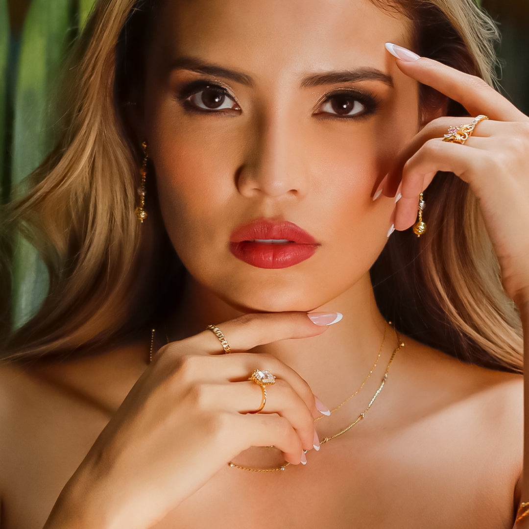 Mano de mujer con anillo en oro amarillo de 18 quilates, con cristal de color blanco cuadrado en el centro y cristales de color blanco alrededor, hecho en Joyería Caracas. 