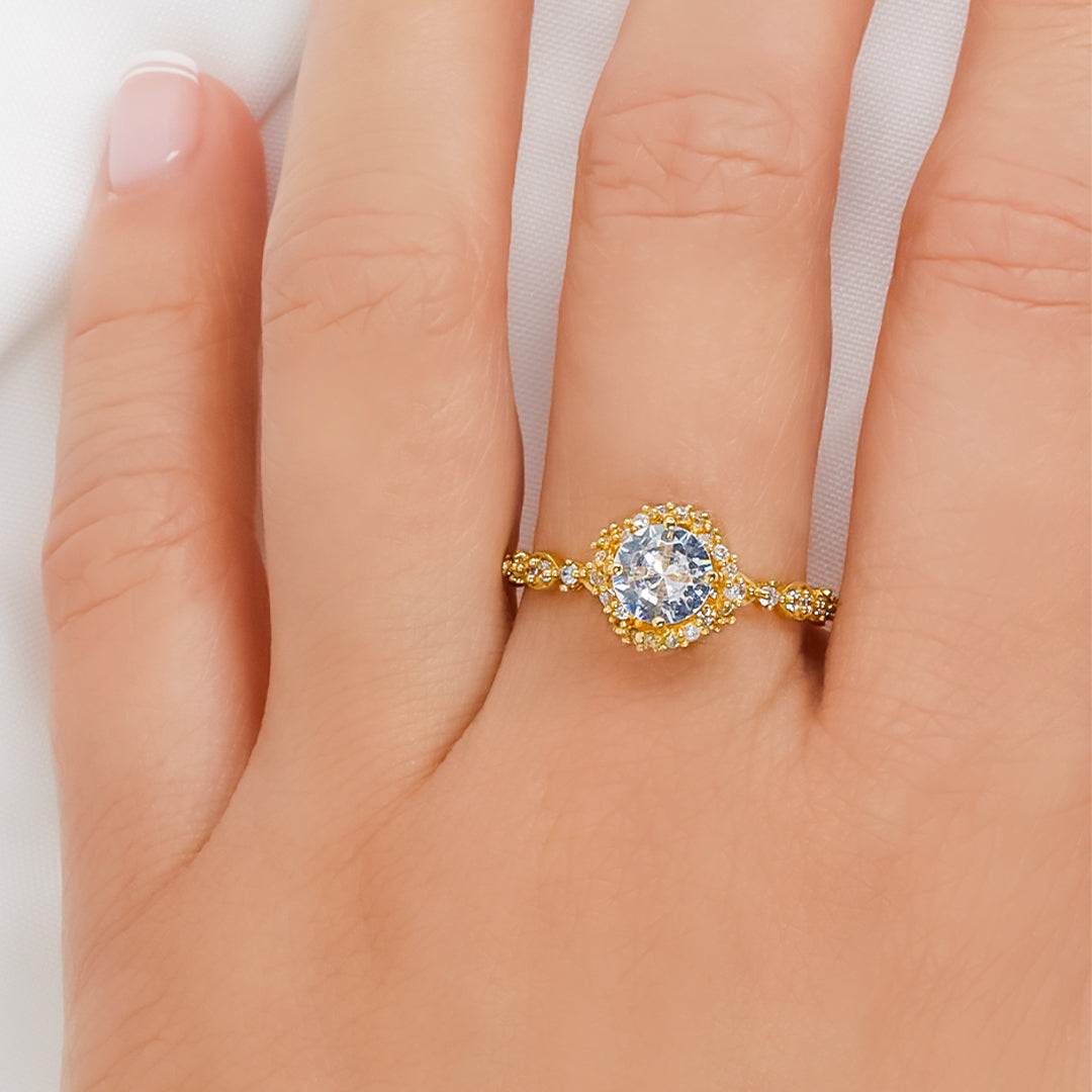 Mano de mujer con anillo en oro amarillo de 18 quilates con un cristal de color blanco en el centro y alrededor, hecho en Joyería Caracas. 