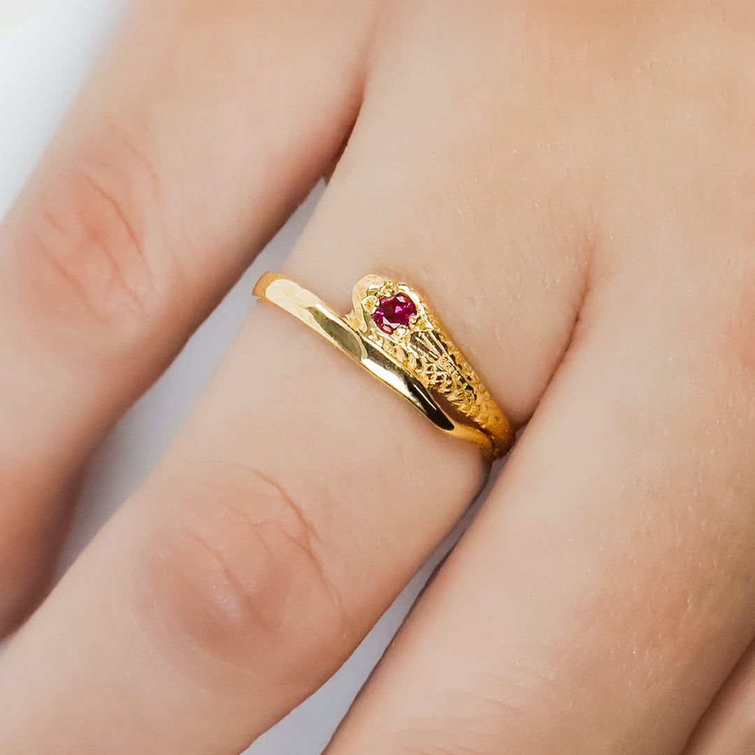 Mano de mujer con anillo en forma de serpiente en oro amarillo de 18 quilates con cristal de color rojo, hecho en Joyería Caracas. 