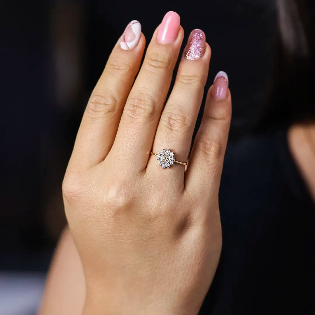 Mano de mujer usando un anillo en oro amarillo de 18 quilates con cristales de color blanco alrededor en el centro grabadas las iniciales de Joyería Caracas.