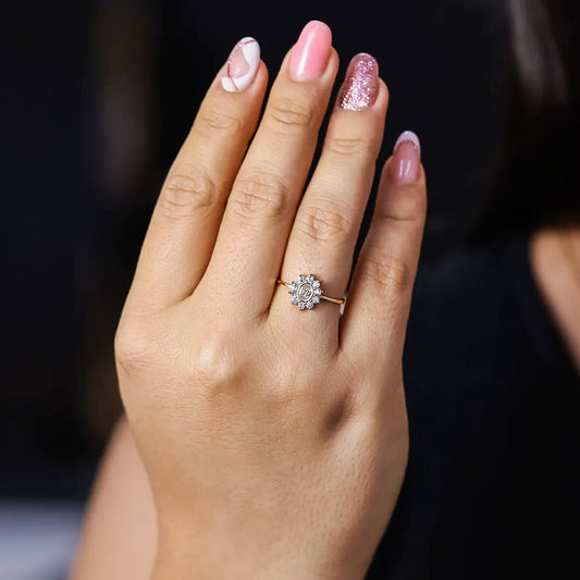 Mano de mujer usando un anillo en oro amarillo de 18 quilates con cristales de color blanco alrededor en el centro grabadas las iniciales de Joyería Caracas.