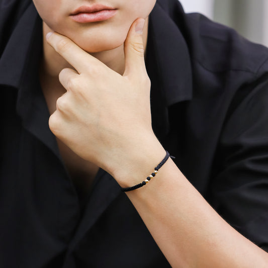 Mano de hombre con pulsera tejida en hilo negro con esferas facetadas en oro amarillo de 18 quilates, hecho en Joyería Caracas. 