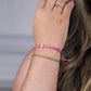 Mano de mujer con pulsera tejida en hilo rosa con accesorios en color rosa y dije de Niña en oro amarillo de 18 quilates. 