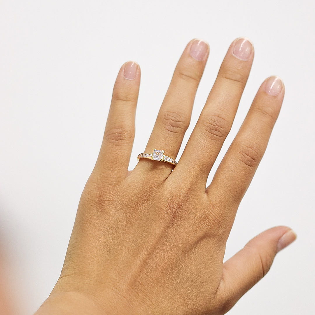 Mano de mujer usando anillo con cuadrado en el centro en oro blanco de 18 quilates y cristales de color blanco, hecho en Joyería Caracas. 