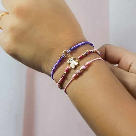 Mano de mujer con pulsera tejida en hilo de colores con esferas lisas y dije en forma de oso en oro amarillo de 18 quilates, hecho en Joyería Caracas. 