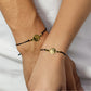 Mano de mujer y hombre con pulsera tejida en hilo negro coreano, dije en forma de Yin y Yang y 2 esferas en oro amarillo de 18 quilates, hecho en Joyería Caracas. 