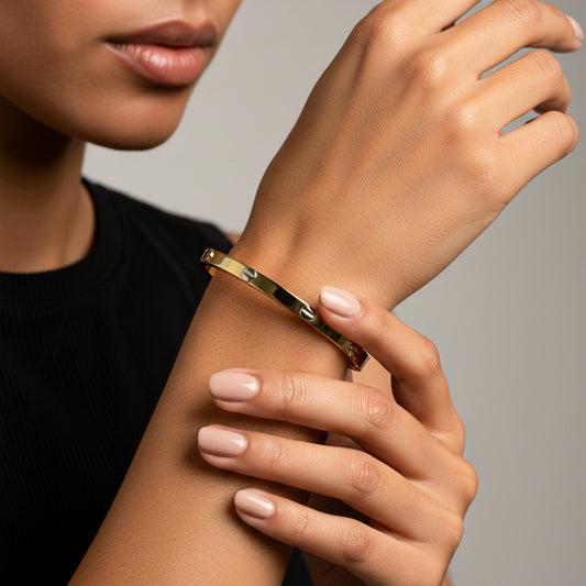 Mano de mujer usando una pulsera de aro en oro amarillo con tornillos en oro blanco de 18 quilates de Joyería Caracas. 