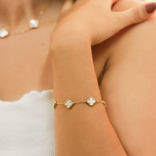 Brazo de mujer con pulsera con formas de tréboles en oro amarillo de 18 quilates y acabados en nácar de color blanco, fabricado por Joyería Caracas. 