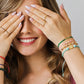 Mano de mujer usando una pulsera tejida en hilo de color rosa con accesorios del mismo color y esfera facetada en el centro en oro amarillo de 18 quilates de Joyería Caracas.