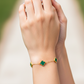 Mano de una modelo usando una pulsera con formas de tréboles en oro amarillo con piedras de nácar verdes de Joyería Caracas.