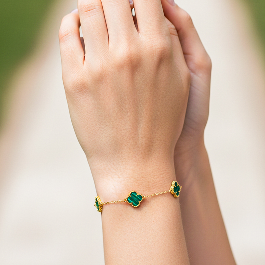 Mano de una modelo usando una pulsera con formas de tréboles en oro amarillo con piedras de nácar verdes de Joyería Caracas.