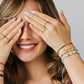 Mano de mujer usando una pulsera tejida en hilo verde con accesorios del mismo color con un herraje en forma de infinito en oro amarillo de 18 quilates con cristales de color verde de Joyería Caracas. 