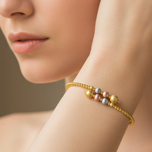 Mano de mujer usando una pulsera brazalete en oro amarillo con esferas diamantadas en oro rosa, amarillo y blanco de 18 quilates de Joyería Caracas.