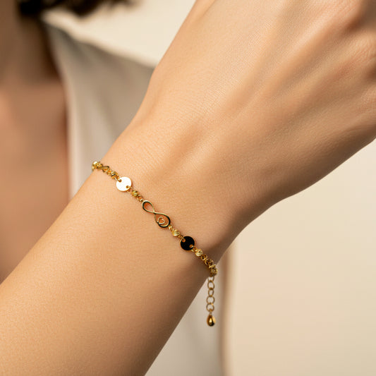 Mano de mujer usando una pulsera con herrajes de infinitos con corazón y esferas facetadas en oro amarillo de 18 quilates de Joyería Caracas. 