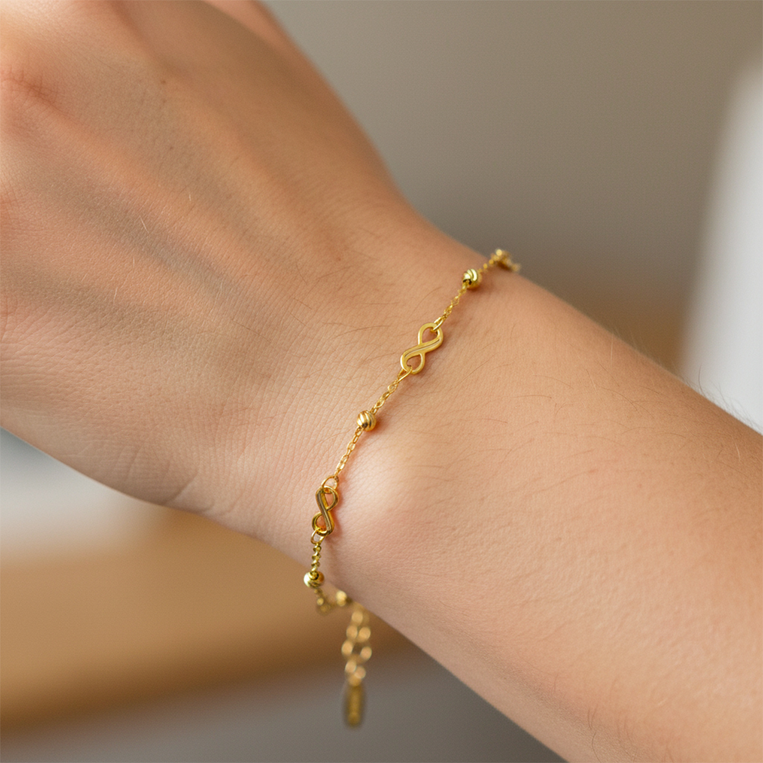 Mano de mujer usando una pulsera con infinitos y esferas facetadas en oro amarillo de 18 quilates de Joyería Caracas. 