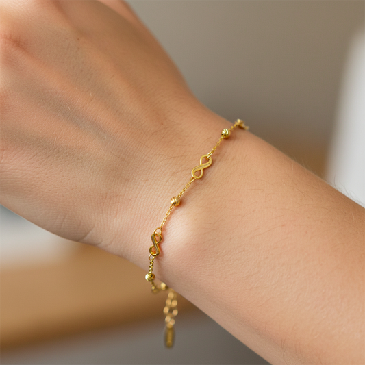 Mano de mujer usando una pulsera con infinitos y esferas facetadas en oro amarillo de 18 quilates de Joyería Caracas. 
