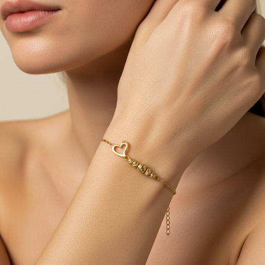 Mano de mujer usando una pulsera con forma de corazón y esferas facetadas en oro amarillo de 18 quilates de Joyería Caracas. 