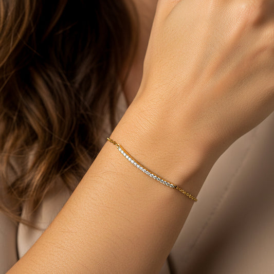 Mano de mujer usando una pulsera en oro amarillo de 18 quilates con cristales de color blanco de Joyería Caracas. 