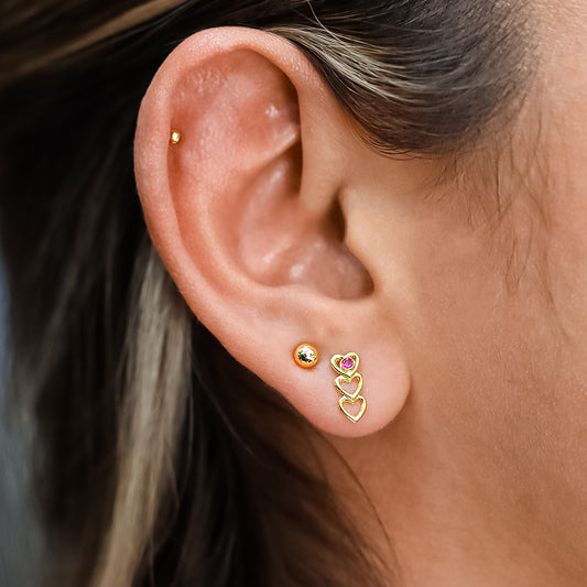 Oreja de mujer con topito de fila de corazones en oro amarillo de 18 quilates con cristal de color rojo, hechos en Joyería Caracas. 