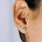 Oreja de mujer usando topito en forma de flor en oro amarillo de 18 quilates con un cristal de color verde en el centro y cristales de color blanco alrededor. 