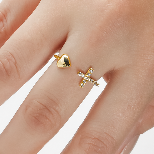 Mano de mujer con anillo en forma de cruz y corazón en oro amarillo de 18 quilates con cristales de color blanco, hecho en Joyería Caracas. 