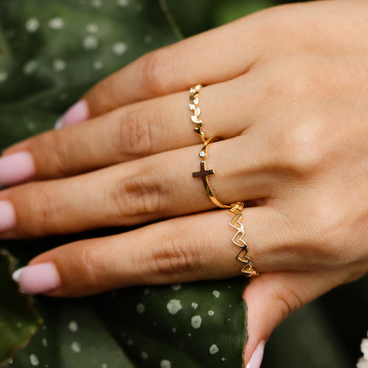 Mano de mujer con anillo en forma de cruz abierta en oro amarillo de 18 quilates y cristal de color blanco, hecho en Joyería Caracas. 