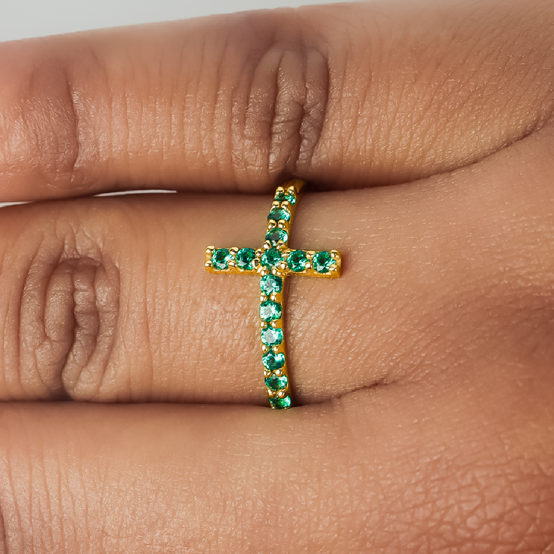 Mano de mujer con anillo en forma de cruz en oro amarillo de 18 quilates con cristales de color verde, hecho en Joyería Caracas. 