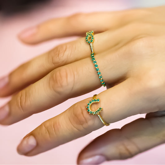 Mano de mujer usando anillo con forma de herradura en oro amarillo de 18 quilates con cristales de color verde, hecho en Joyería Caracas. 
