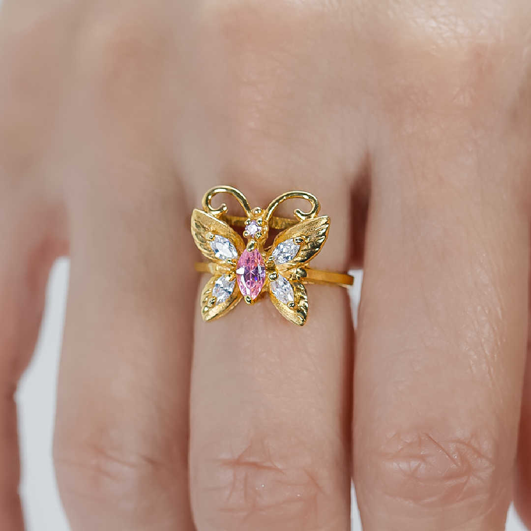 Mano de mujer con anillo en forma de mariposa en oro amarillo de 18 quilates con cristales en corte marquise color blanco y rosa, hecho en Joyería Caracas. 