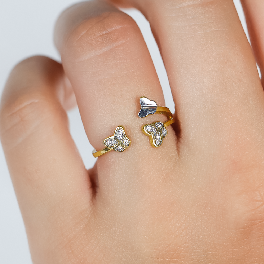 Mano de mujer con anillo en forma de mariposas en oro amarillo y blanco de 18 quilates con cristales de color blanco, hecho en Joyería Caracas. 