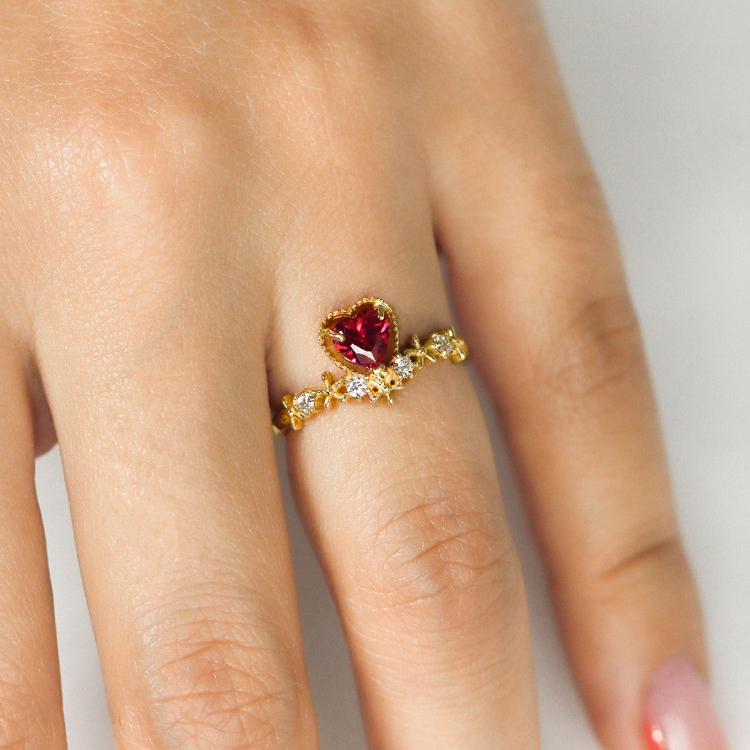 Mano de mujer con anillo en oro amarillo de 18 quilates con cristal de color rojo en forma de corazón y cristales circulares de color blanco, hecho en Joyería Caracas. 