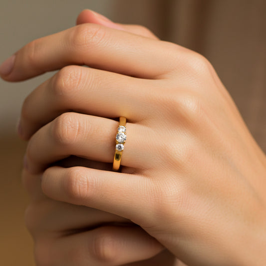 Mano de mujer usando un anillo en oro amarillo de 18 quilates con 3 piedras de color blanco de Joyería Caracas. 