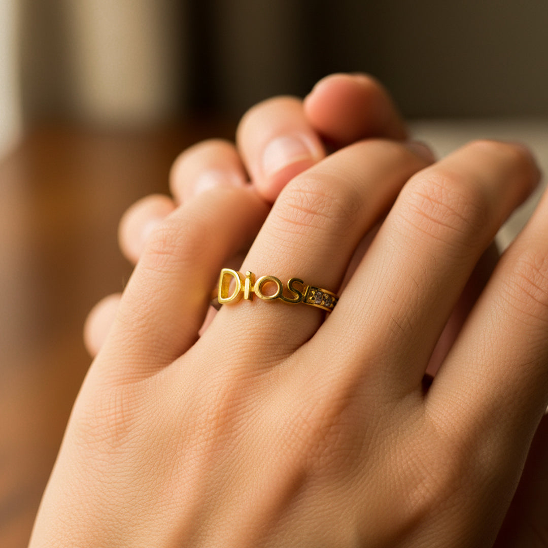 Mano de mujer usando un anillo con la palabra Dios en oro amarillo de 18 quilates y cristales de color blanco de Joyería Caracas. 