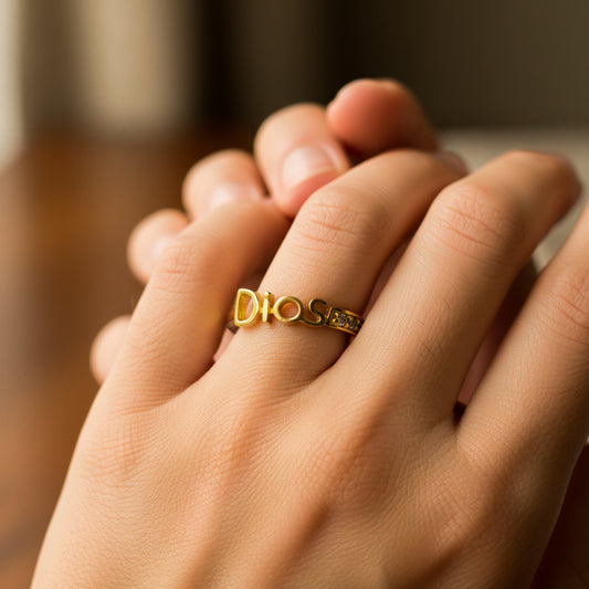 Mano de mujer usando un anillo con la palabra Dios en oro amarillo de 18 quilates y cristales de color blanco de Joyería Caracas. 