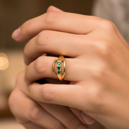 Mano de mujer usando un anillo en oro amarillo de 18 quilates en forma de bucle con cristales de color verde de Joyería Caracas. 