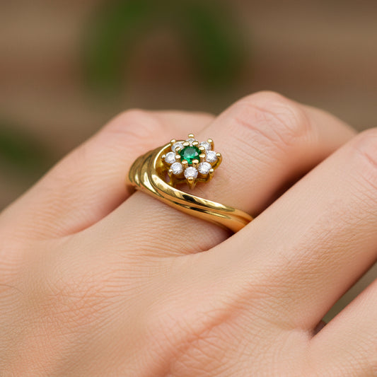 Mano de mujer usando un anillo con forma de onda con flor en oro amarillo de 18 quilates con Esmeralda y Diamantes de Joyería Caracas. 