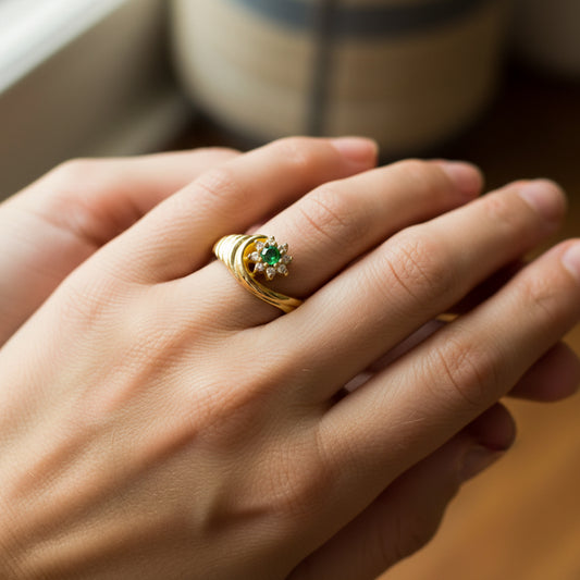 Mano de mujer usando un anillo en forma de concha con flor en oro amarillo de 18 quilates con cristales de color verde y blanco de Joyería Caracas. 