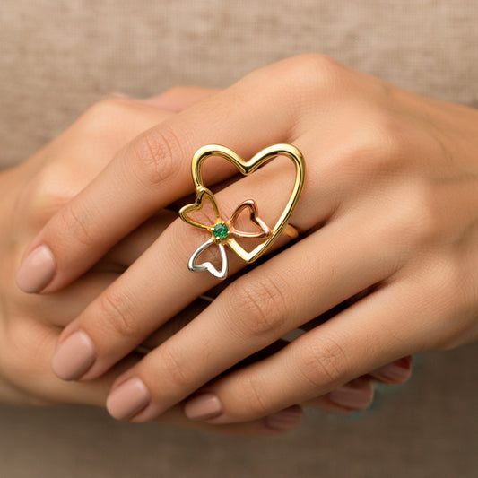 Mano de mujer usando un anillo con forma de corazón y trébol 3 oros de 18 quilates con cristal de color verde de Joyería Caracas. 