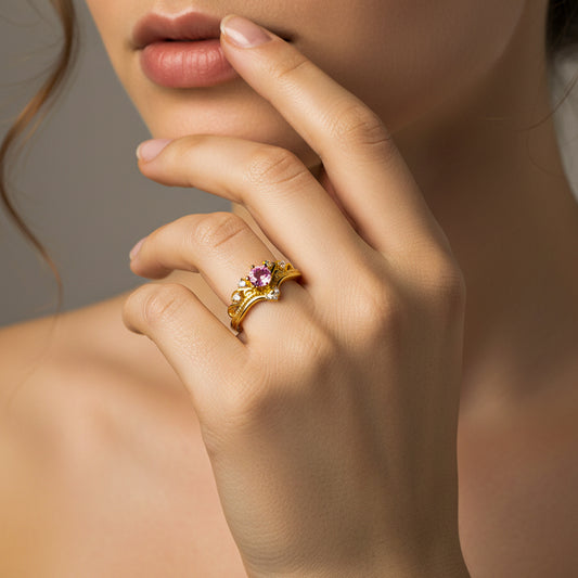 Mano de mujer usando un anillo en forma de corona inglesa en oro amarillo de 18 quilates con cristales de color blanco y 1 rosa en el centro de Joyería Caracas. 