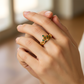 Mano de mujer usando un anillo en forma de corona en oro amarillo de 18 quilates con cristales de color verde de Joyería Caracas. 