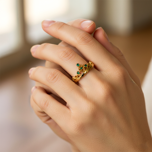 Mano de mujer usando un anillo en forma de corona en oro amarillo de 18 quilates con cristales de color verde de Joyería Caracas. 