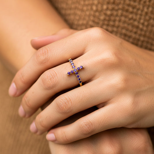 Mano de mujer usando un anillo con forma de cruz en oro amarillo de 18 quilates con cristales de color morado de Joyería Caracas. 