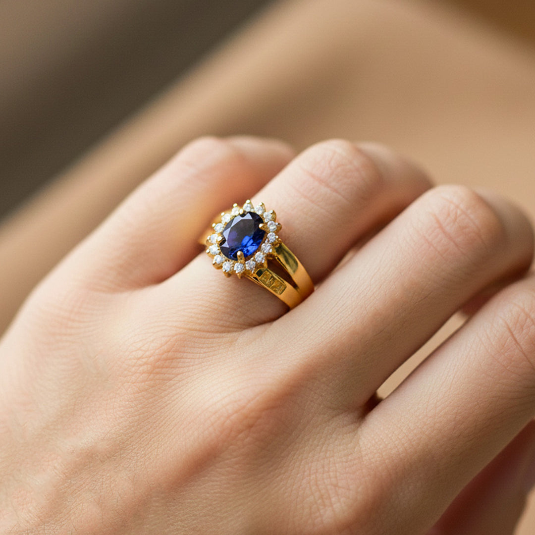 Mano de modelo usando un anillo de grado con diseño de Lady Di en oro amarillo de 18 quilates con cristal ovalado azul y blancos alrededor de Joyería Caracas. 
